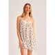A woman modeling a white semi-sheer slip dress with black polka dots and a lace-trimmed neckline, photographed against a plain light gray studio background.