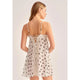 A woman shown from the back wearing a white slip-style nightgown with dark brown polka dots and lace trim at the back, photographed against a plain light gray studio background.