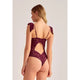 A woman shown from the back wearing a burgundy lace bodysuit with shoulder bows and a large open back cutout, photographed against a plain light gray studio background.