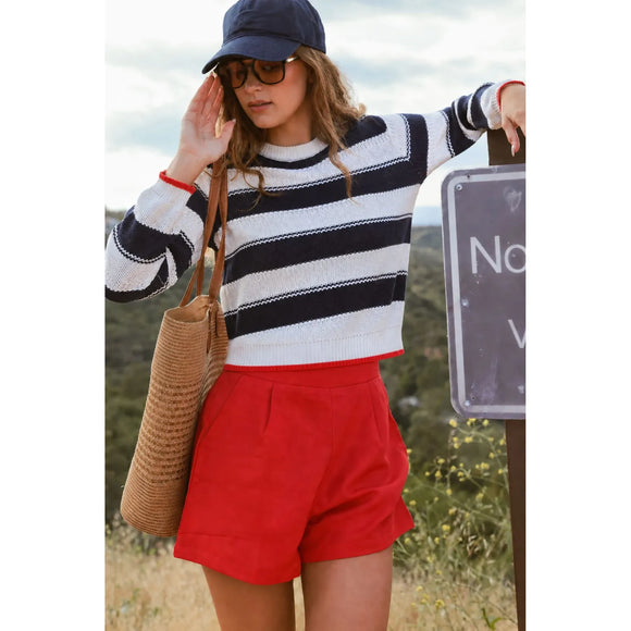 Woman in striped sweater and red shorts standing outdoors near a sign.