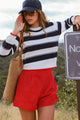Woman in striped sweater and red shorts standing outdoors near a sign.