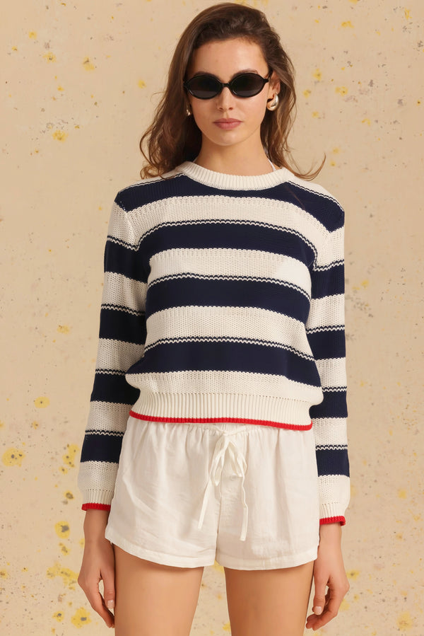 Woman wearing a striped sweater and white shorts on a beige background