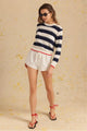 Woman wearing a striped sweater and white shorts on a beige background