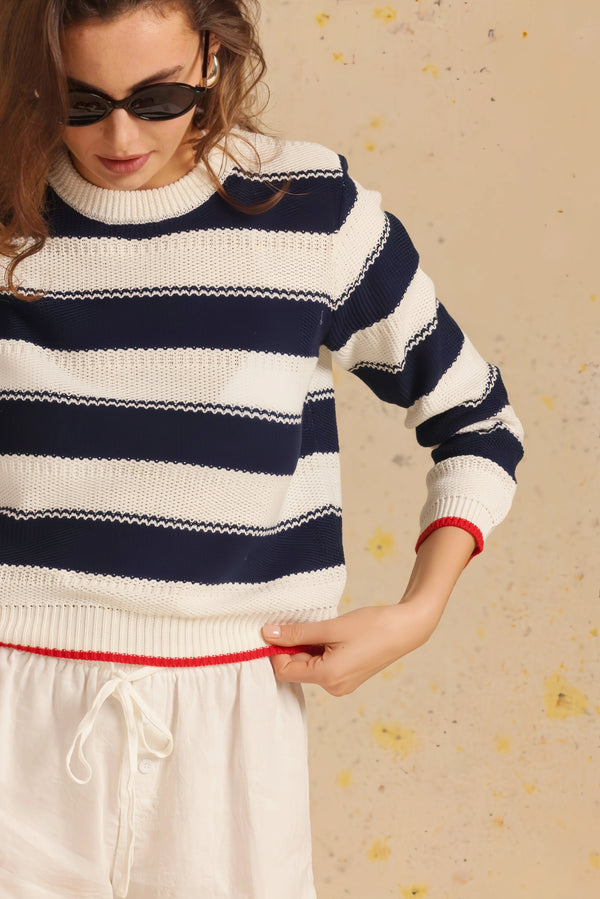 Person wearing a navy and white striped sweater with a red trim on a beige background.