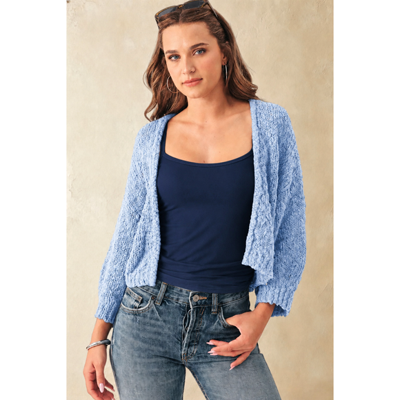 Woman wearing a blue cardigan over a navy top and jeans against a beige background