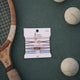 Vintage tennis racket and balls on a green surface with a Klanc hair ties packaging.