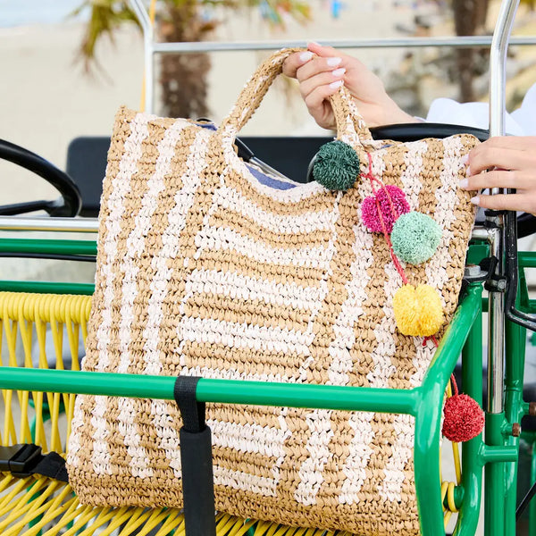Woven bag with colorful pom-poms held by a person on a green and yellow vehicle.