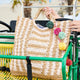 Woven bag with colorful pom-poms held by a person on a green and yellow vehicle.