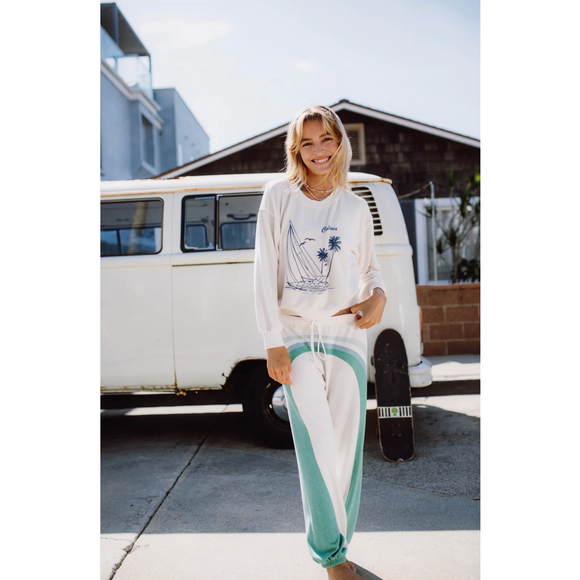 Person wearing a white shirt with a graphic design and light blue pants standing in front of a white van.