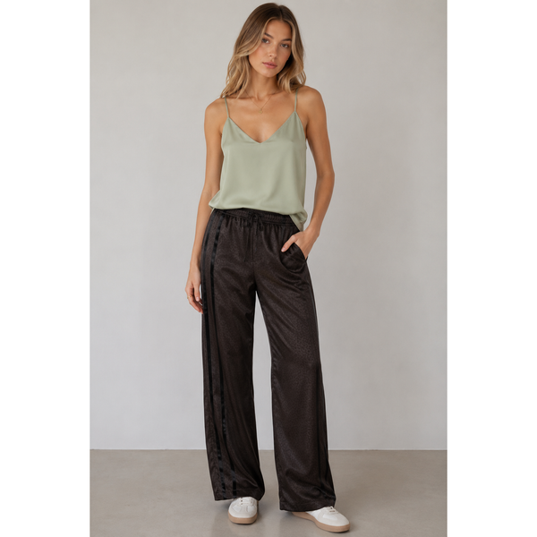 Woman wearing a light green tank top and black wide-leg pants against a plain background