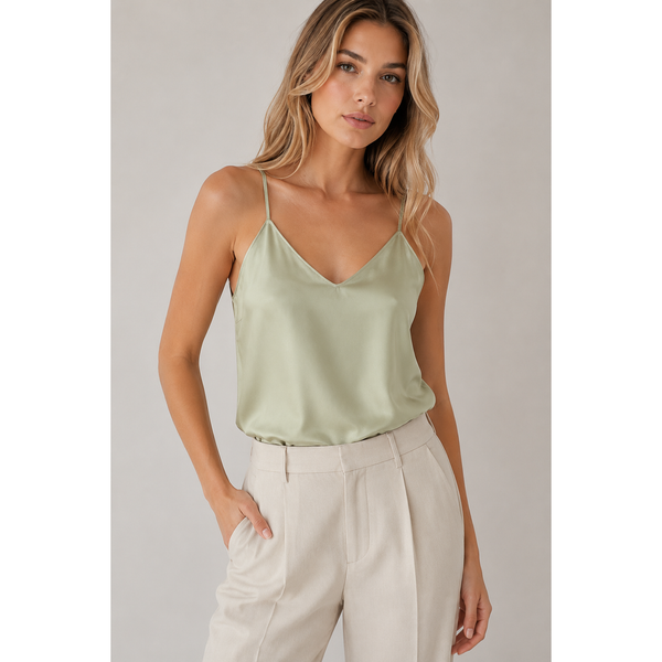 Woman wearing a light green satin camisole and beige pants against a plain background