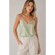 Woman wearing a light green satin camisole and beige pants against a plain background