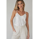 Woman wearing a white spaghetti strap top and beige pants against a plain background
