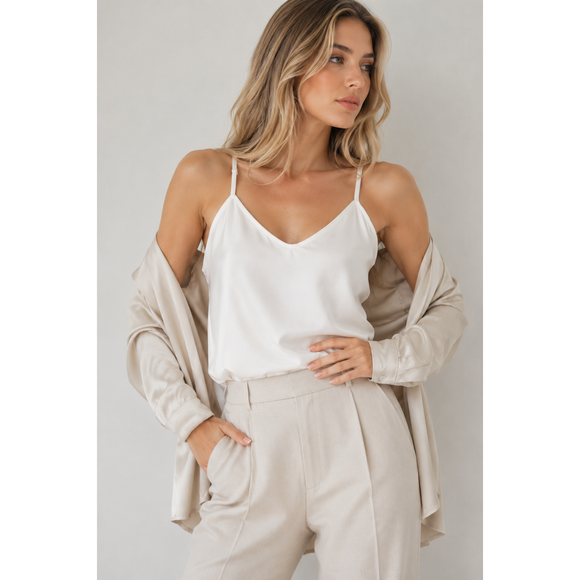 Woman wearing a white top and beige pants with a beige cardigan on a plain background