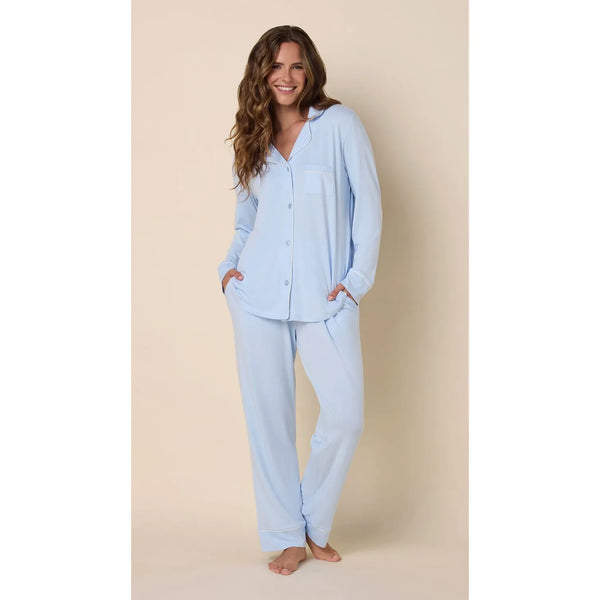 A woman modeling a light blue long-sleeve button-front pajama top and matching loose pajama pants against a plain beige studio background.