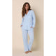 A woman modeling a light blue long-sleeve button-front pajama top and matching loose pajama pants against a plain beige studio background.