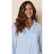 A woman with long wavy brown hair wearing a light blue pajama shirt with white piping, shown against a solid beige background.