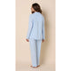 A woman wearing a light blue two-piece pajama set, consisting of a long-sleeve button-up top and matching pants, shown from a rear three-quarter view against a solid beige studio background.