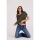 A woman kneeling on a light gray studio floor wearing an olive green oversized short-sleeve crop top and blue jeans with a black belt.