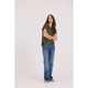 A woman stands barefoot against a plain light gray studio background, wearing a loose olive green short-sleeve top and blue jeans with a slight flare at the hem.