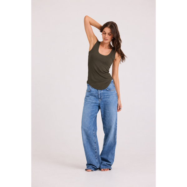 A woman modeling a dark olive green scoop-neck tank top and wide-leg blue jeans against a plain white studio background.