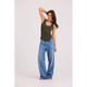 A woman modeling a dark olive green scoop-neck tank top and wide-leg blue jeans against a plain white studio background.