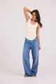 A woman modeling a cream-colored ribbed tank top and wide-leg blue jeans against a plain white studio background.