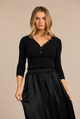 A woman modeling a black long-sleeve henley top with a gathered elastic waist and a flowing black skirt, set against a solid beige studio background.