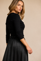 A woman modeling a black long-sleeve henley top with a gathered elastic waist and a flowing black skirt, set against a solid beige studio background.