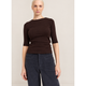 A woman modeling a dark brown 3/4-sleeve crewneck top and dark navy wide-leg trousers, standing against a plain light beige wall.