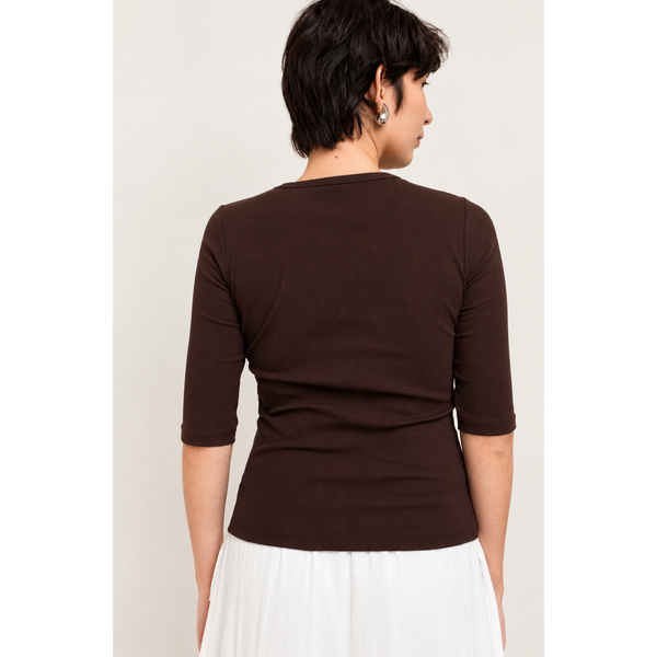 A woman shown from the back wearing a dark brown 3/4-sleeve top and a white skirt, against a plain light background.
