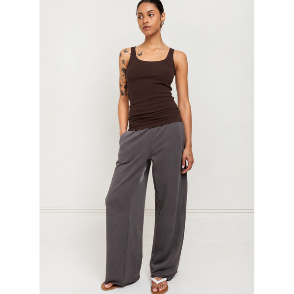 A woman modeling a dark brown ribbed tank top and wide-leg charcoal gray pants against a plain white studio background.