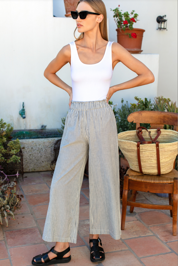 Woman wearing a white tank top and striped pants standing on a patio.