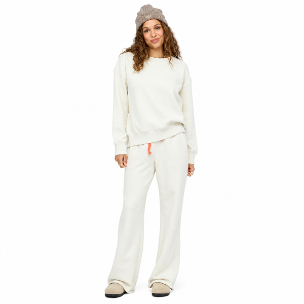 A woman modeling a matching cream sweatshirt and wide-leg sweatpants lounge set, styled with a beige knit beanie and beige slip-on shoes against a solid white background.