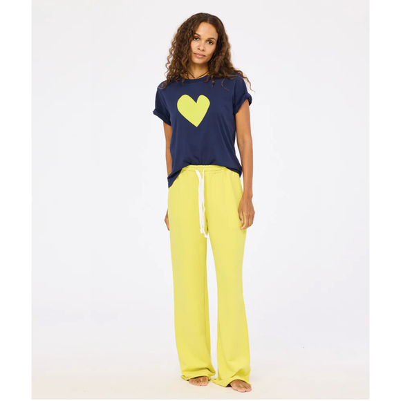 Woman wearing a navy t-shirt with a yellow heart and yellow pants on a white background