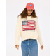 Person wearing a cream sweater with an American flag design, blue jeans, and a pink cap with a heart on a white background.