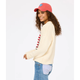 Woman wearing a cream sweater, red cap, and blue jeans on a white background