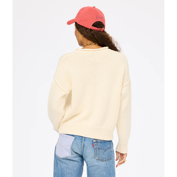 Person wearing a light-colored sweater and blue jeans with a pink cap on a white background