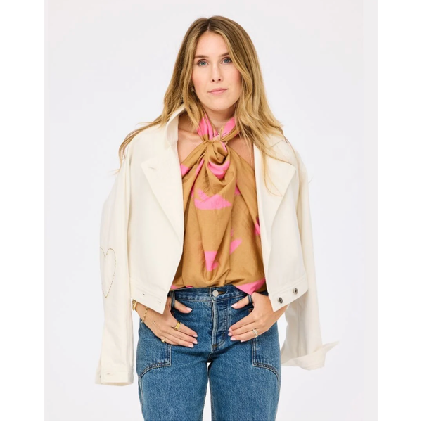 Woman wearing a beige jacket, pink blouse, and blue jeans on a white background