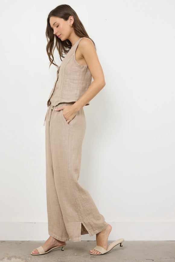 Woman wearing a beige sleeveless top and wide-leg pants against a white background