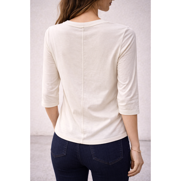 Person wearing a white long-sleeve top and dark jeans against a plain background