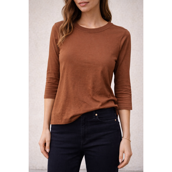 Woman wearing a brown long-sleeve top and black pants against a neutral background