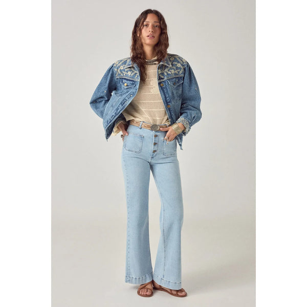 Woman wearing a denim jacket, beige sweater, and light blue jeans on a plain background