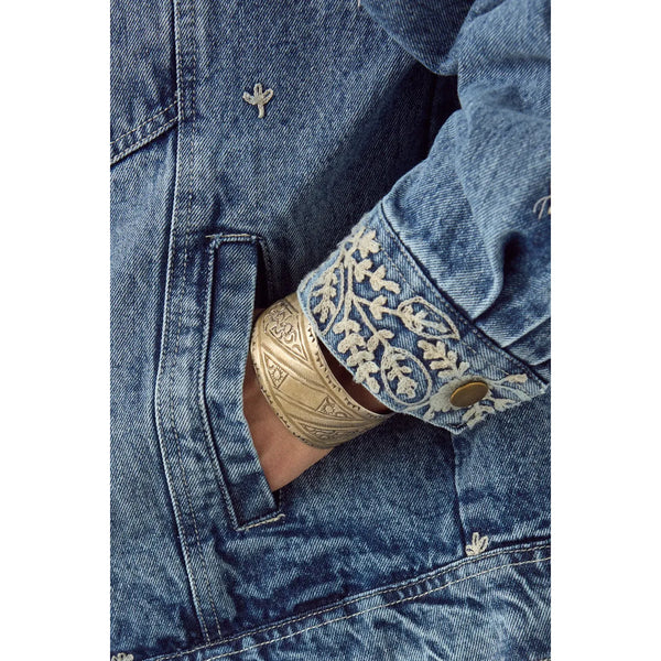 Close-up of a blue denim jacket with embroidered cuffs and a gold bracelet.