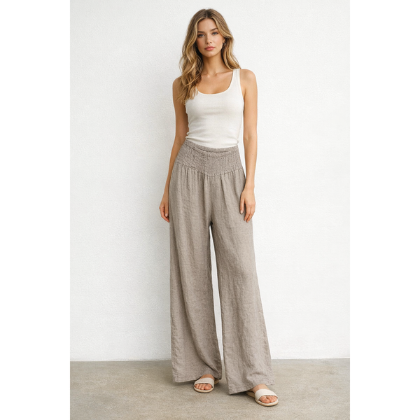 Woman wearing a white tank top and beige wide-leg pants on a plain background