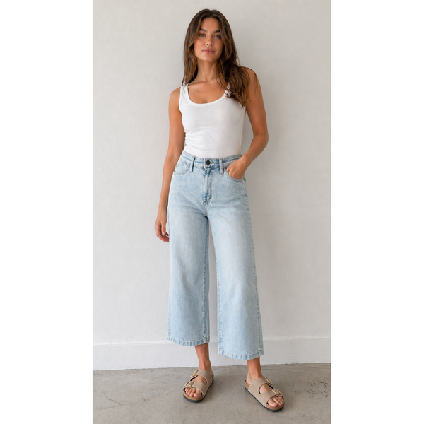 Woman wearing a white tank top and light blue jeans against a plain background