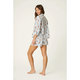 A woman modeling a matching pajama set consisting of a long-sleeve button-up shirt and shorts, featuring a white base with thin blue vertical stripes and a repeating brown teddy bear print, set against a plain light beige studio background.
