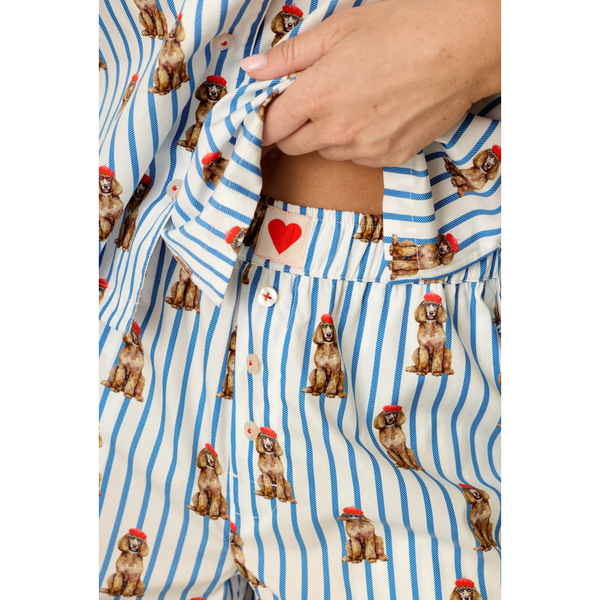 Close-up of a person wearing blue and white striped pajama pants with a repeating print of poodles wearing red hats, and a matching top partially visible.