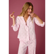 A woman modeling a light pink pajama set with a small green leaf pattern, holding a glass and a lollipop against a solid pink background.