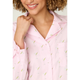 A close-up of a woman wearing a light pink pajama shirt with a repeating green and yellow cocktail glass print. The image shows her smiling, with her hand near her collarbone, highlighting the collar and fabric texture.
